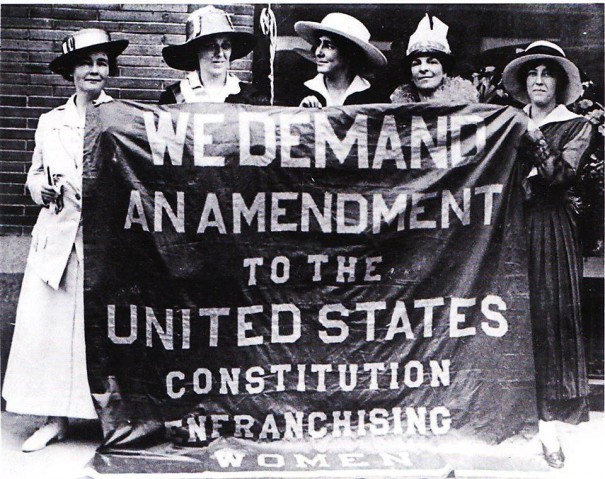 Ann Martin (far left) and Sara Bard Field (far right) pose behind the "Great Demand" banner of the Congressional Union for Woman Suffrage.