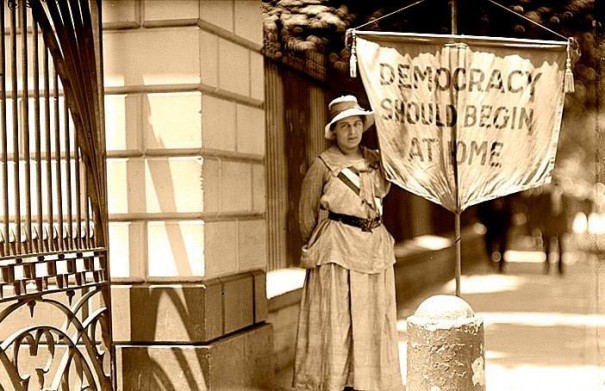 Betty Gram, of Portland, Oregon, picketing along the White House fence carrying a banner reminding President Wilson that "DEMOCRACY SHOULD BEGIN AT HOME."